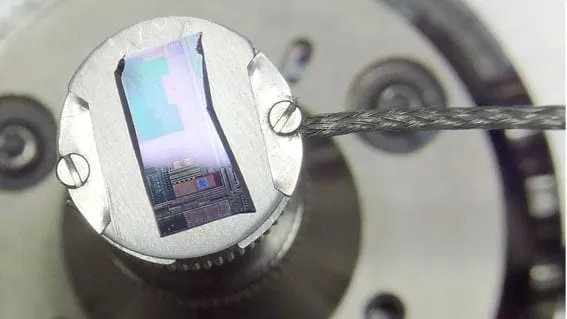 The MHS mounted on a rotating sample holder disc inside a deposition or FIB chamber, surrounded by clamps and cabling.