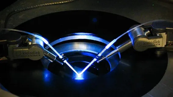 Two pipette tips converging on a single point in a recording dish, lit by a blue laser beam crossing between them.