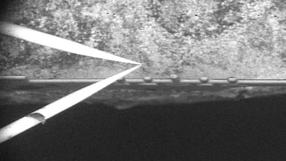 SEM image of a sharp manipulator probe lifting a thin lamella away from a trench during in-situ lift-out.