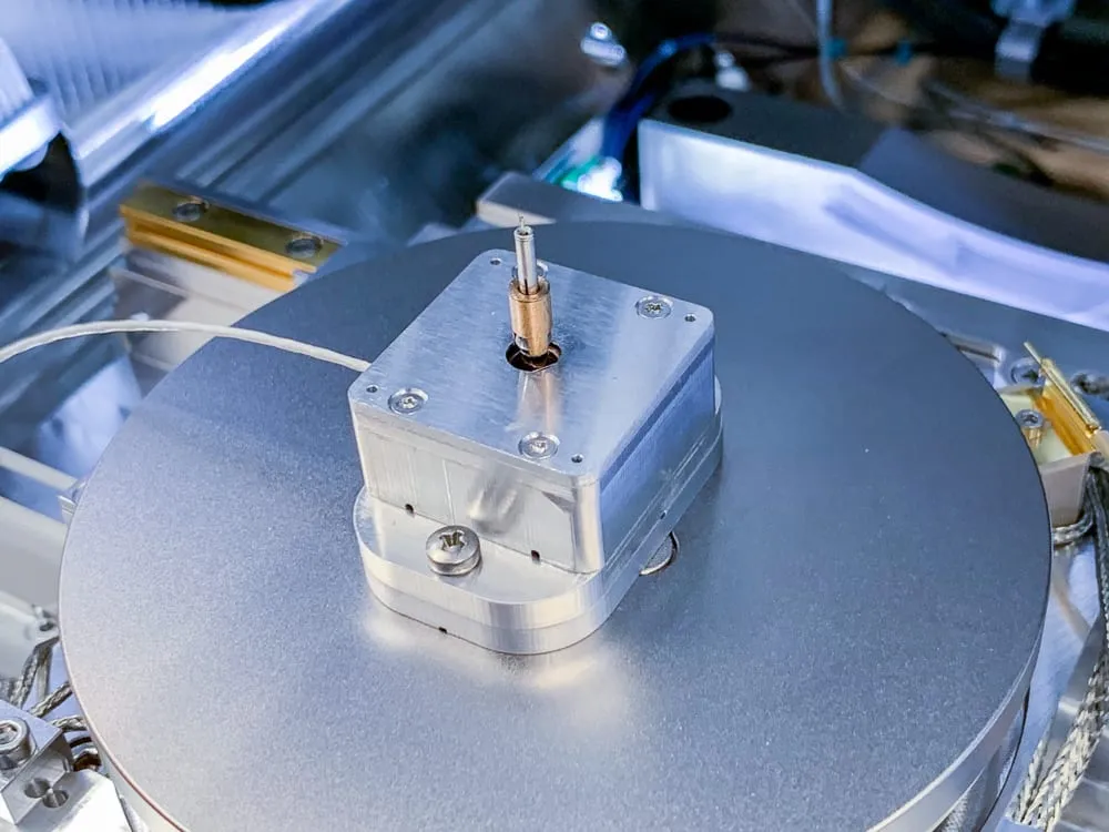 The nanolathe's collet and pin mounted on top of a much larger rotation stage, dwarfed by the disc beneath it.