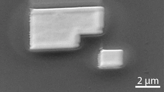 SEM image of a tungsten structure deposited with the GIS-EM, showing a stepped block and a smaller separate pad, 2 µm scale bar.